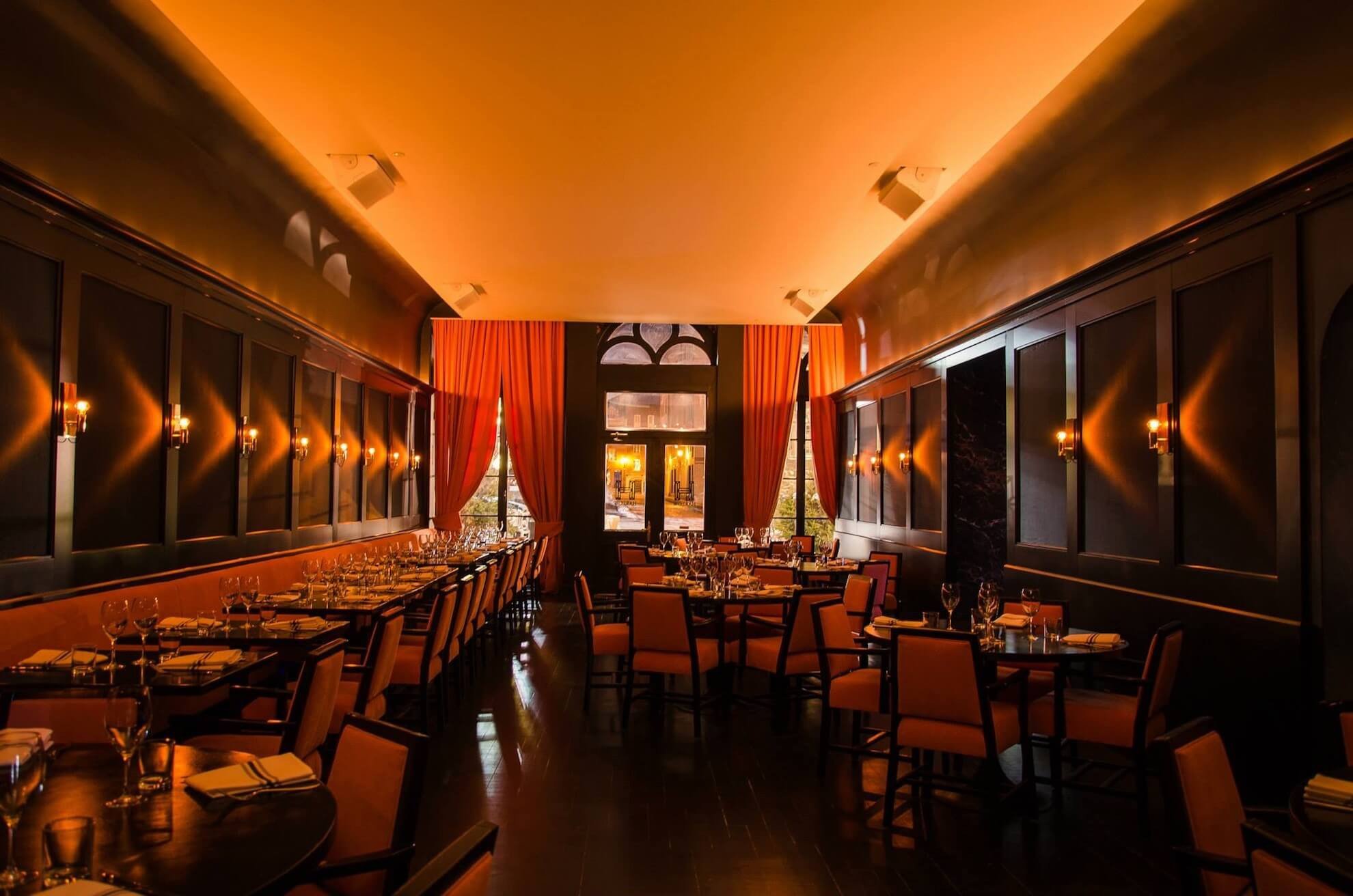 Intérieur de restaurant élégant avec boiseries en bois foncé, chaises orange et éclairage chaleureux.