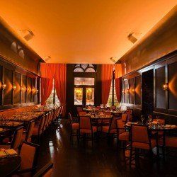 Vue intérieure d'un restaurant avec de longues tables, un éclairage orange et de grandes fenêtres avec des rideaux.