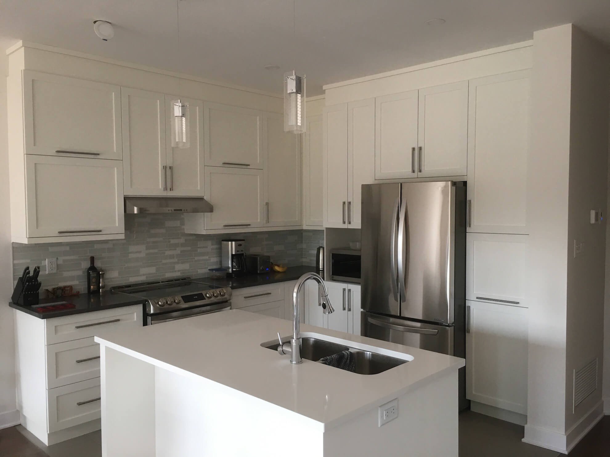 Cuisine blanche moderne avec appareils électroménagers en acier inoxydable, îlot et luminaires.