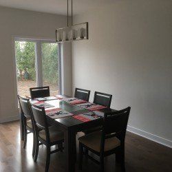 Salle à manger avec table et chaises en bois foncé, sets de table, fenêtre et lustre.