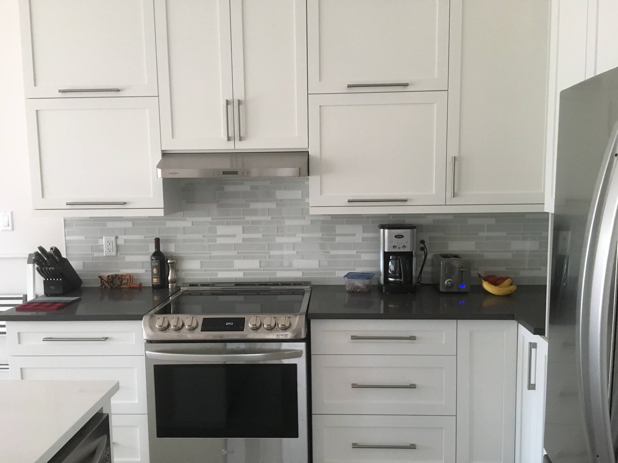 Cuisine blanche avec électroménagers en acier inoxydable et comptoirs foncés.