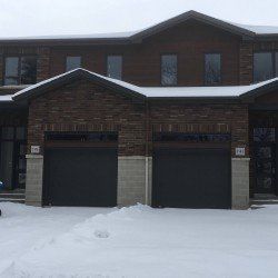 Deux maisons de ville avec portes de garage gris foncé et extérieurs en briques dans un décor enneigé.
