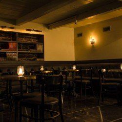 Bar faiblement éclairé avec poutres en bois, étagères et tables avec lanternes éclairées aux bougies.