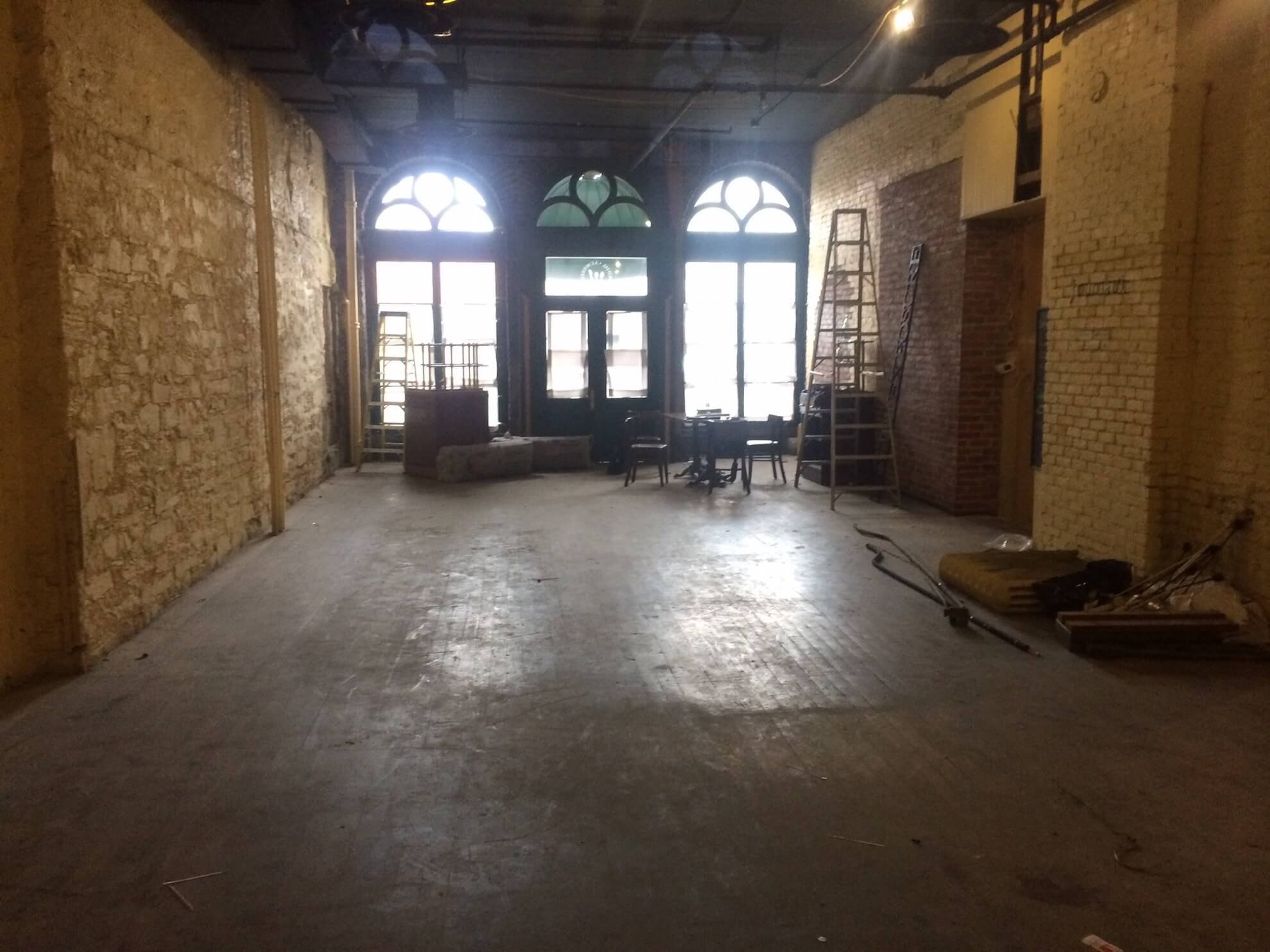 Intérieur vide avec fenêtres cintrées, murs en briques et pierres apparentes, sol en béton.