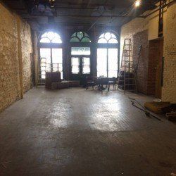 Pièce vide avec fenêtres cintrées, murs en briques et planchers en bois.