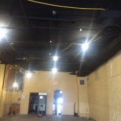 Intérieur d'un bâtiment avec plafond apparent et lumières vives. Les murs sont beiges, vides et en construction.