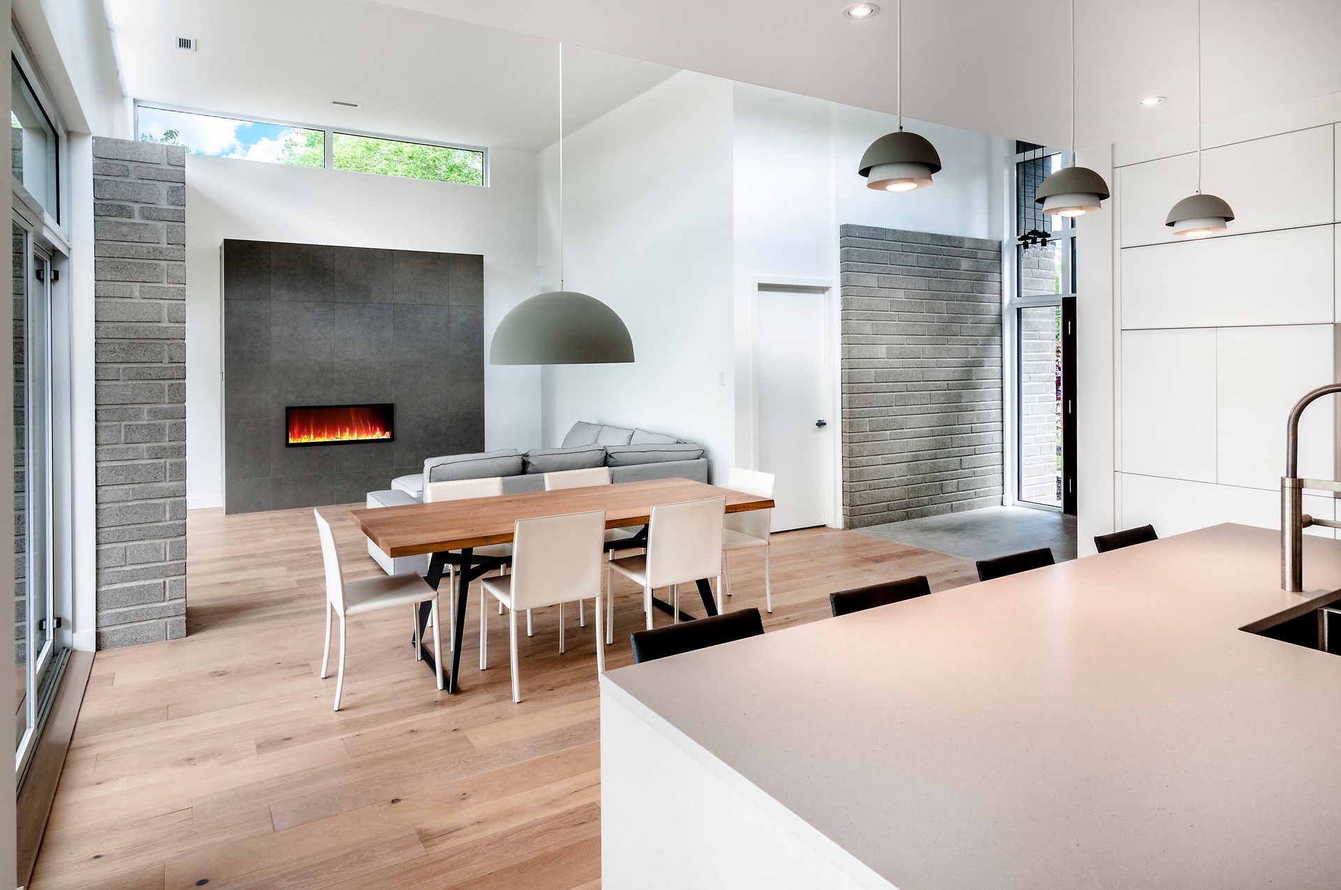 Un espace de vie lumineux et moderne à aire ouverte avec parquet clair, cheminée en pierre, table à manger et cuisine minimaliste.