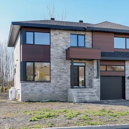 Maison à deux étages avec façade en pierre, revêtement brun foncé et porte de garage noire.