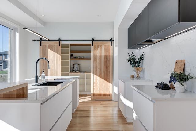Cuisine moderne avec armoires blanches, planchers en bois et portes de grange coulissantes.