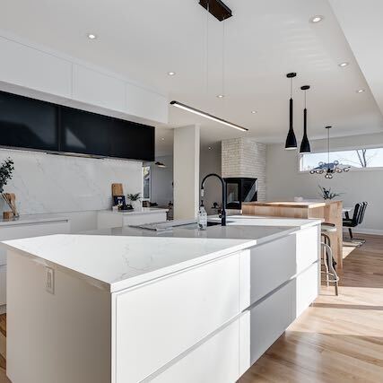 Cuisine blanche moderne avec grand îlot, accents noirs et planchers de bois.