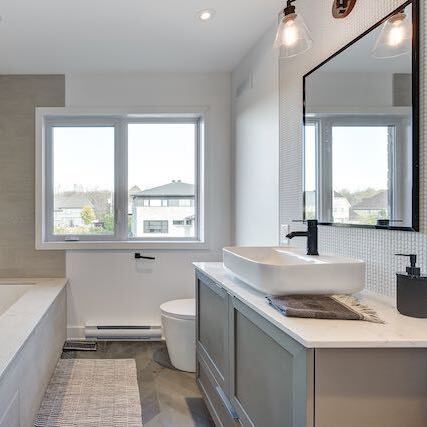 Salle de bain avec lavabo blanc, miroir et fenêtre; vanité et murs gris; luminaires.
