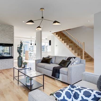 Séjour avec cheminée, canapé gris, table basse et escalier avec parquet en bois clair et luminaire noir.