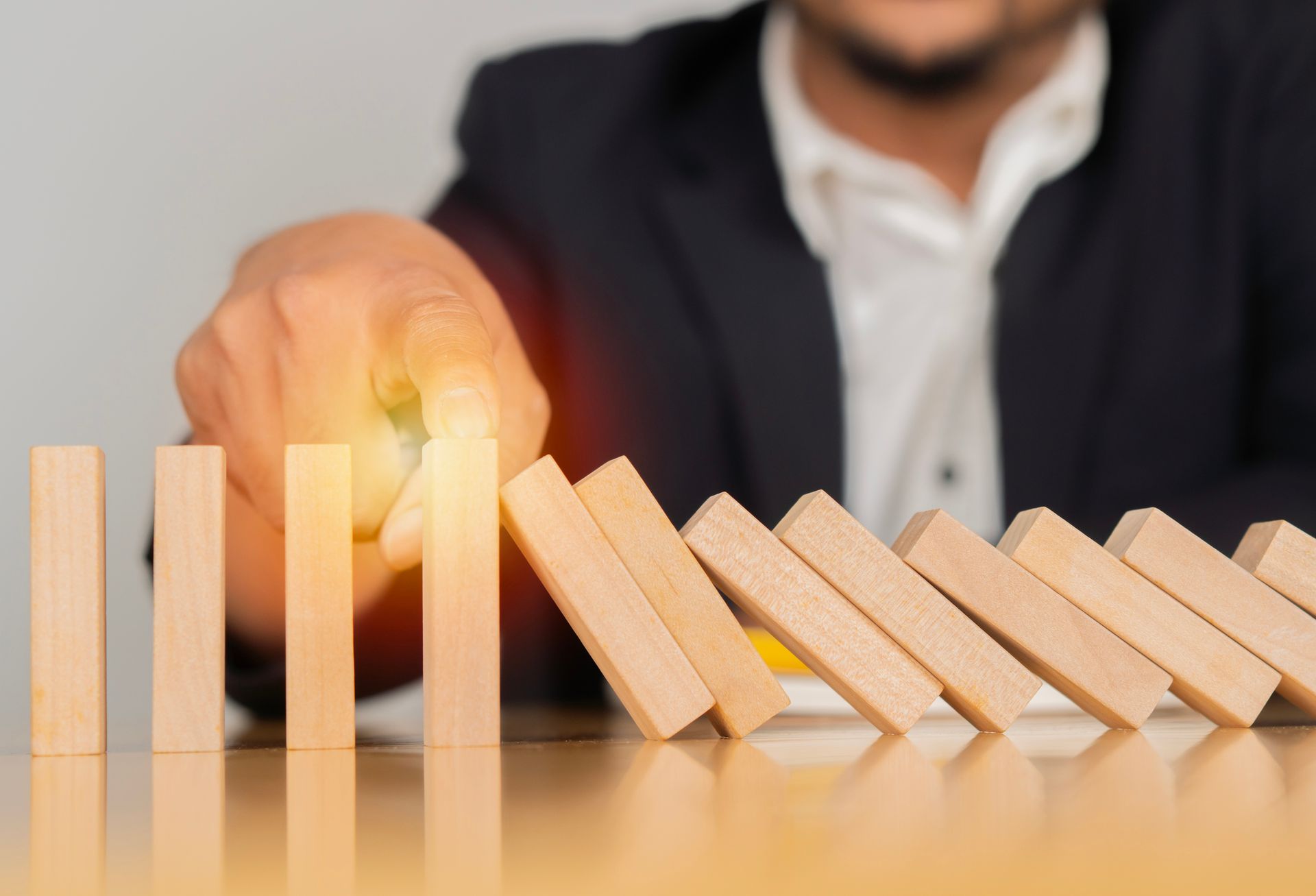 Hand stopping falling wooden domino blocks on a table.