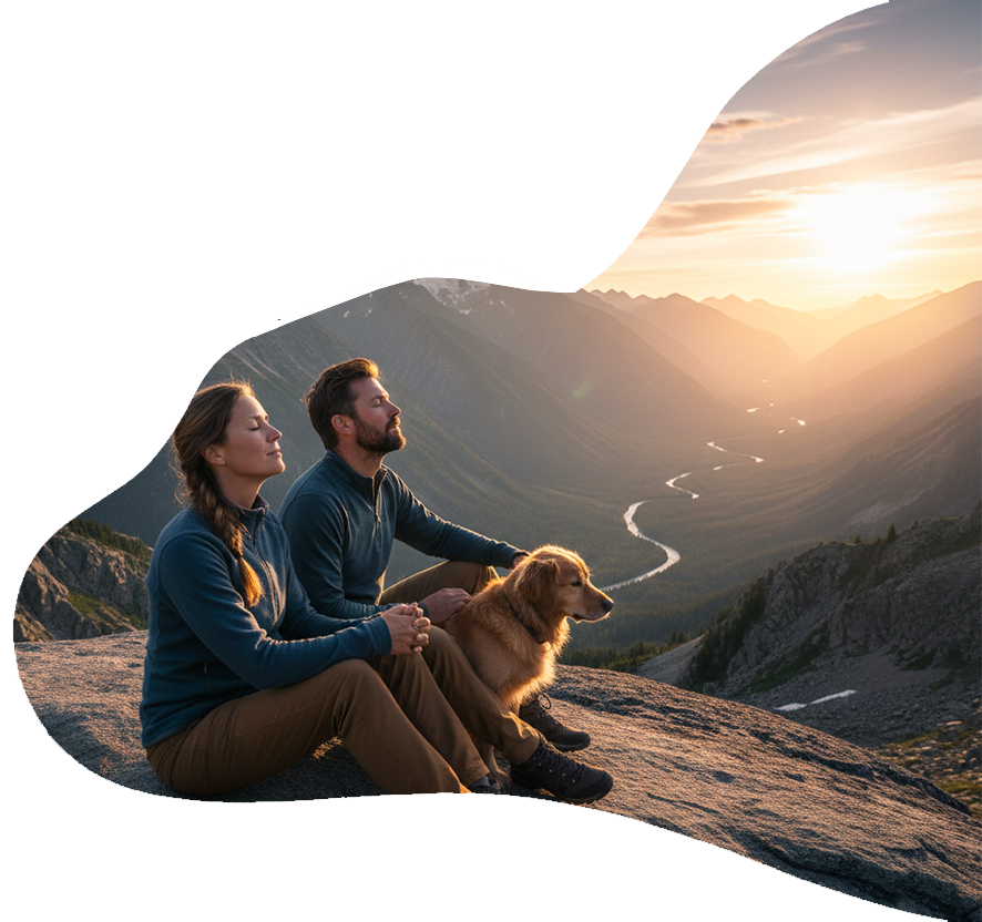 Una coppia e il suo cane sono seduti sulla cima di una montagna e si godono il tramonto sulla valle.