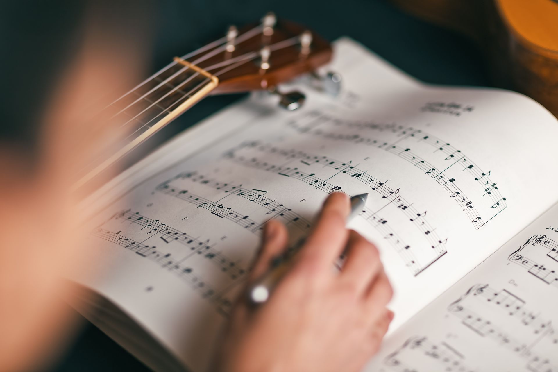 Hands turning pages of sheet music beside a guitar neck