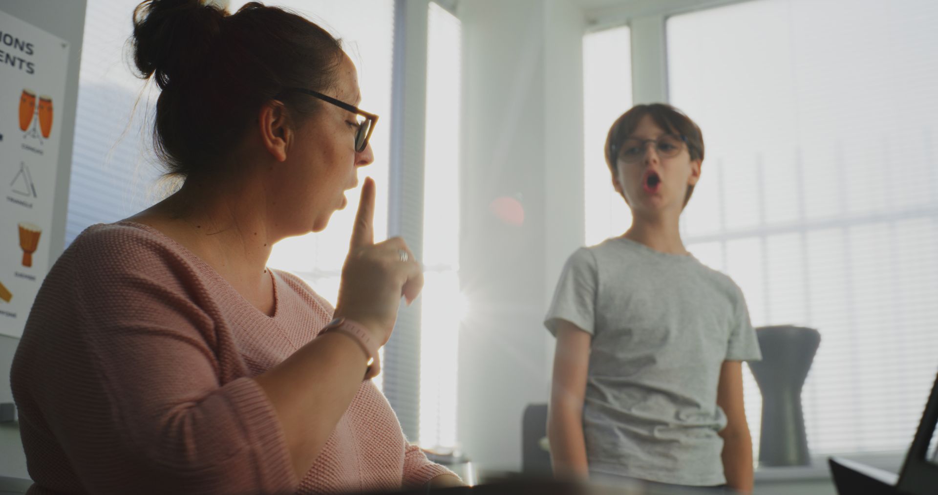 Two people talking in a bright office; one gestures while seated, the other stands nearby.