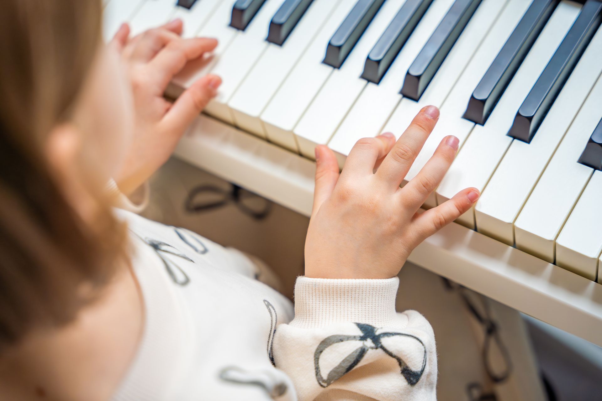 Child playing piano keys close-up, hands on white and black keys
