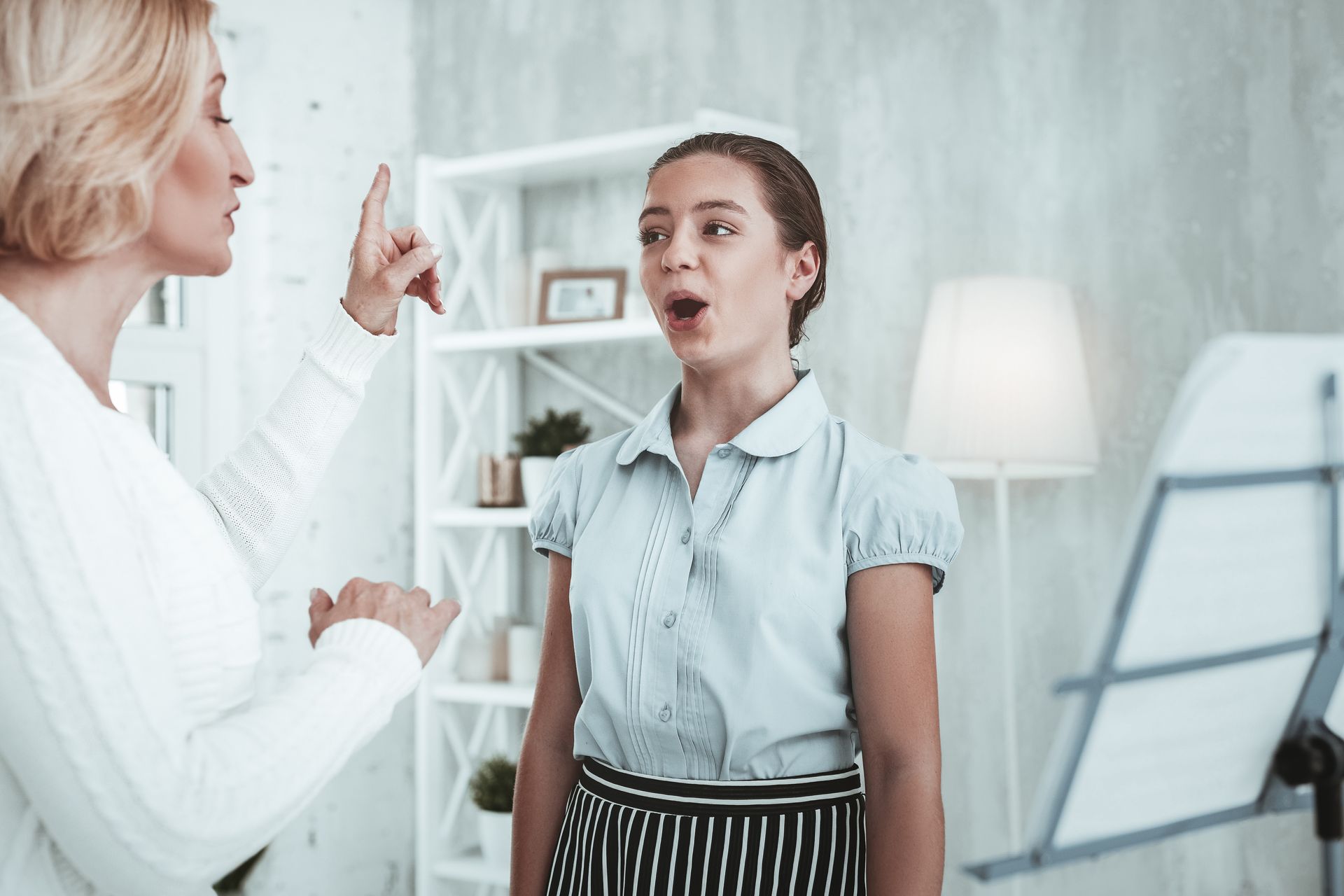 Two women talking in a bright office, one gesturing while the other listens near a whiteboard.