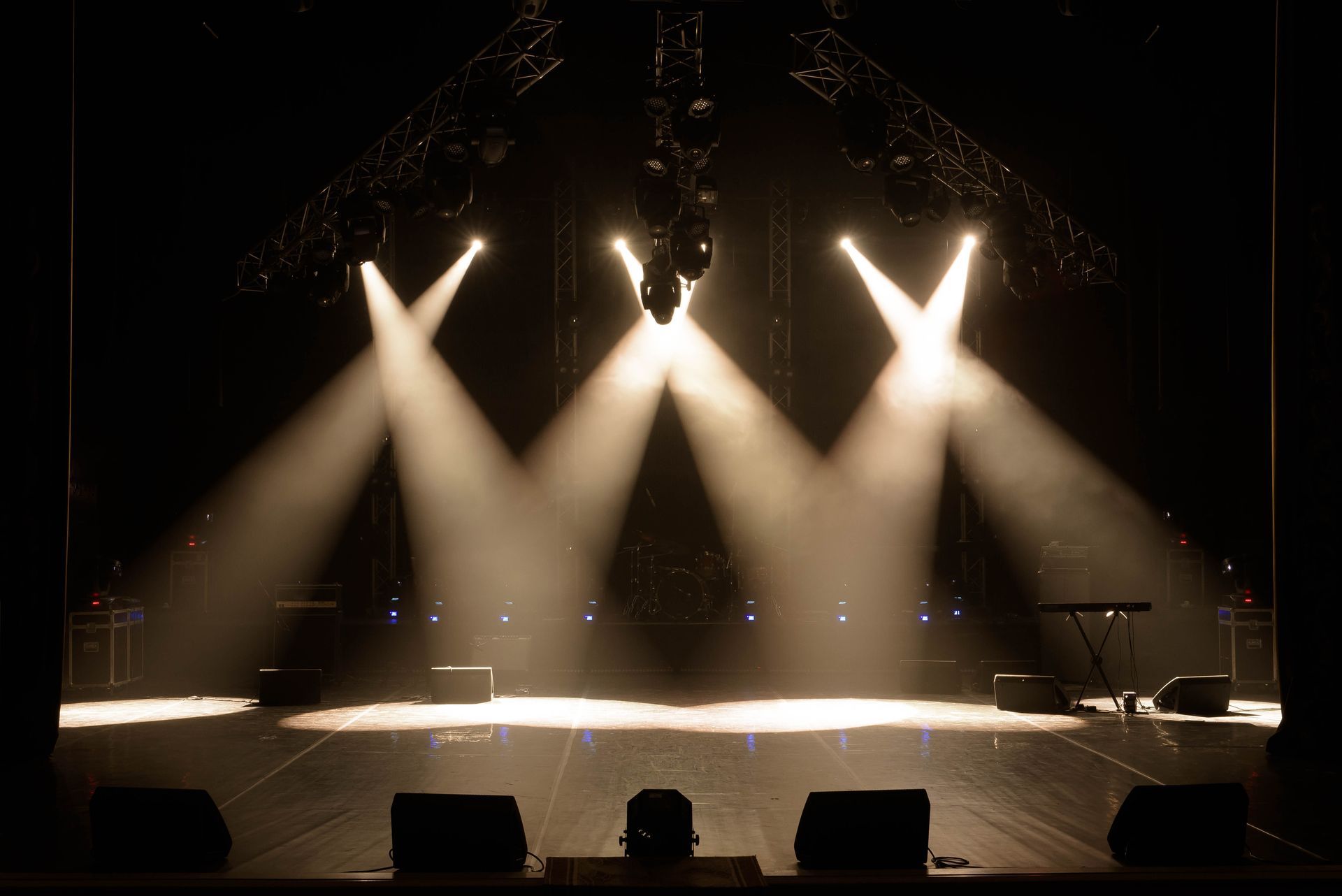 Empty concert stage lit by three bright spotlights in a dark venue
