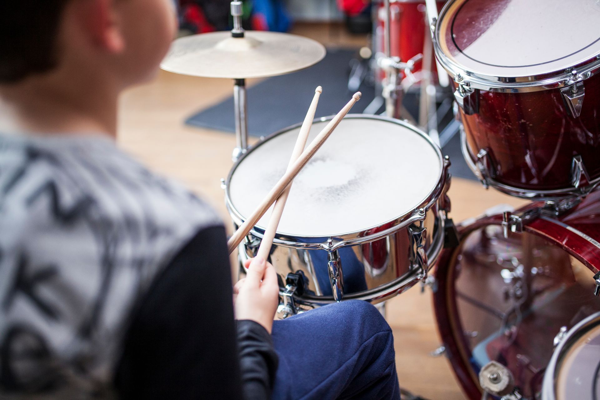 Drummer playing a snare drum with sticks beside a red drum kit