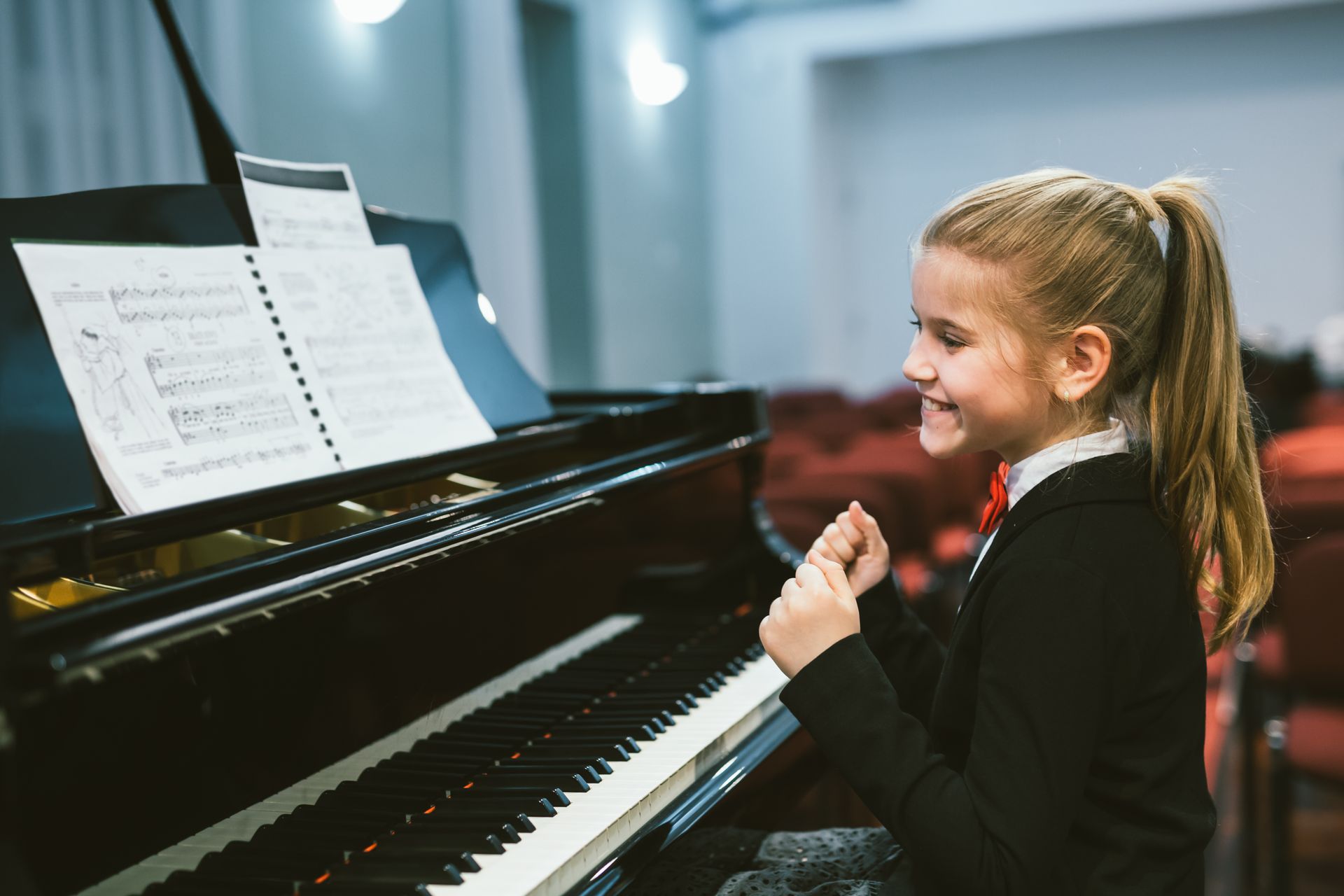 Young girl smiling at a piano while reading sheet music in a bright music room