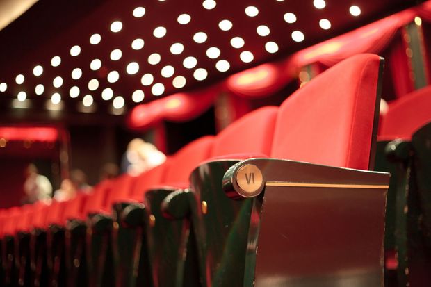 Red theater seats under rows of glowing ceiling lights in a dim auditorium Red theater seats under rows of glowing ceiling lights in a dim auditorium