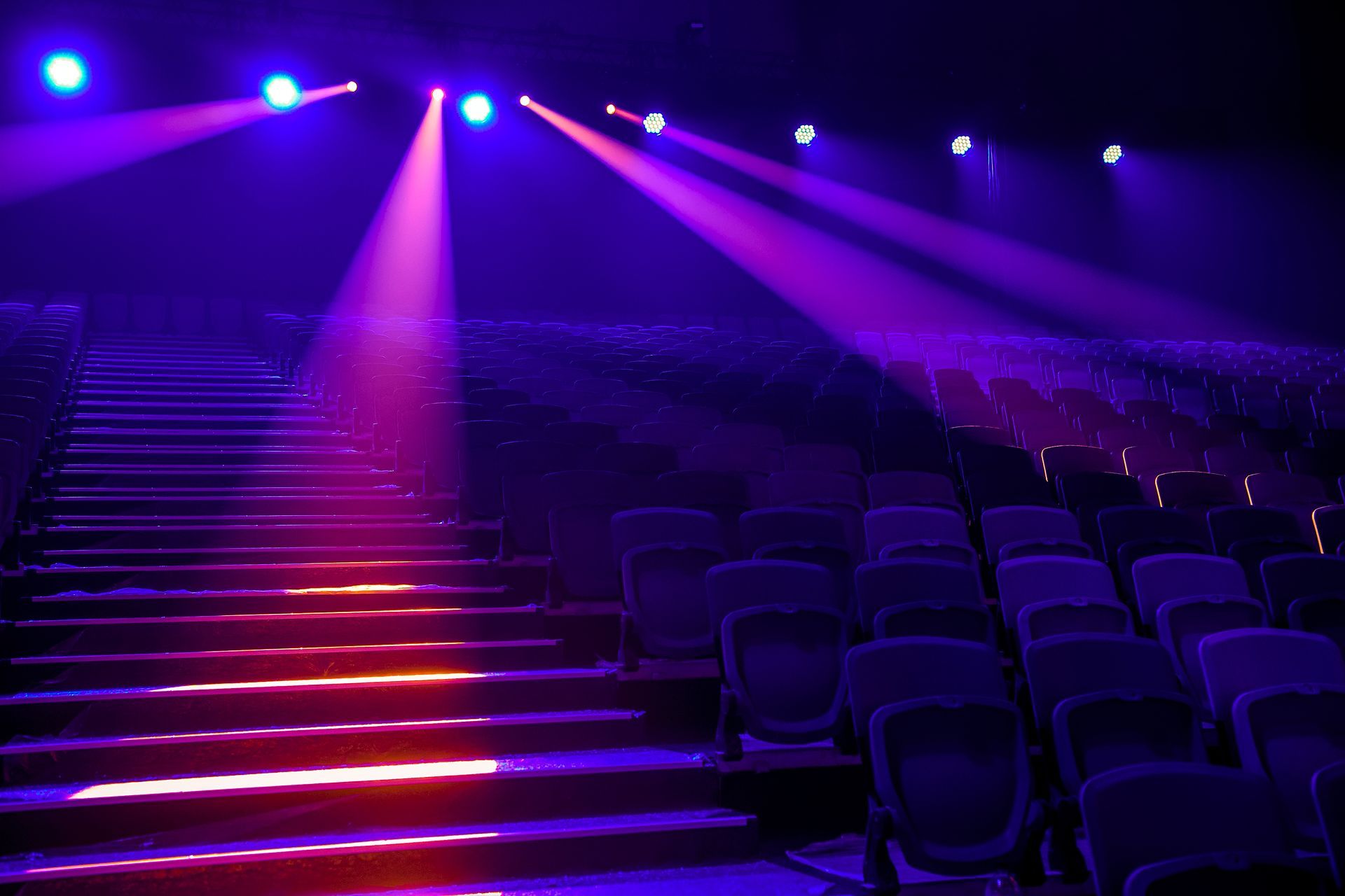 Empty theater seats under purple stage lights with illuminated stairs