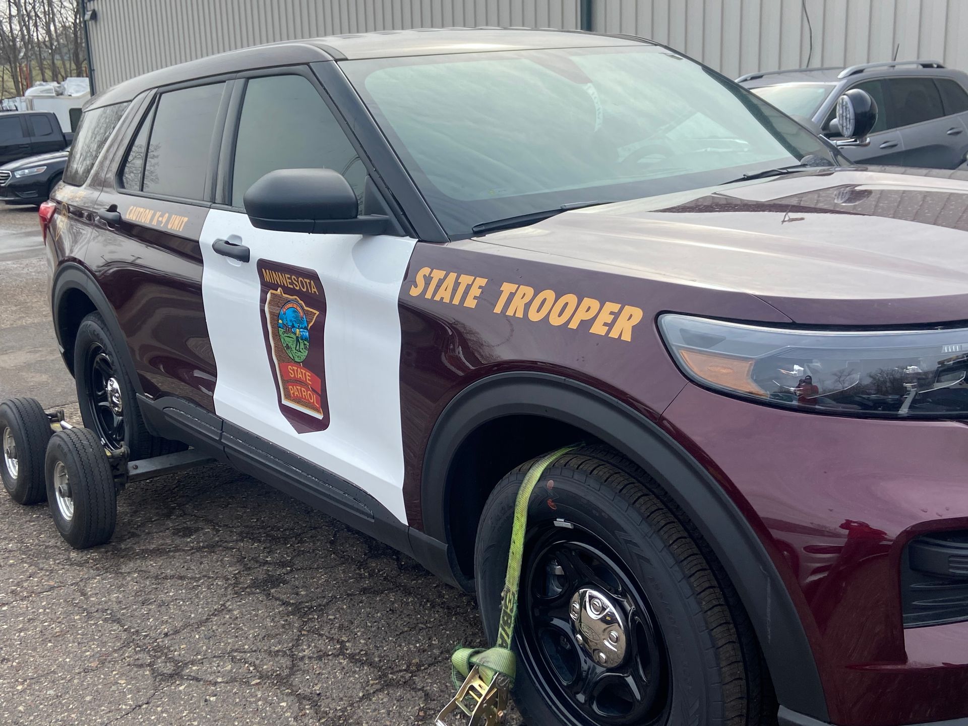 Maroon and white state trooper SUV with a flat tire, parked in a lot.