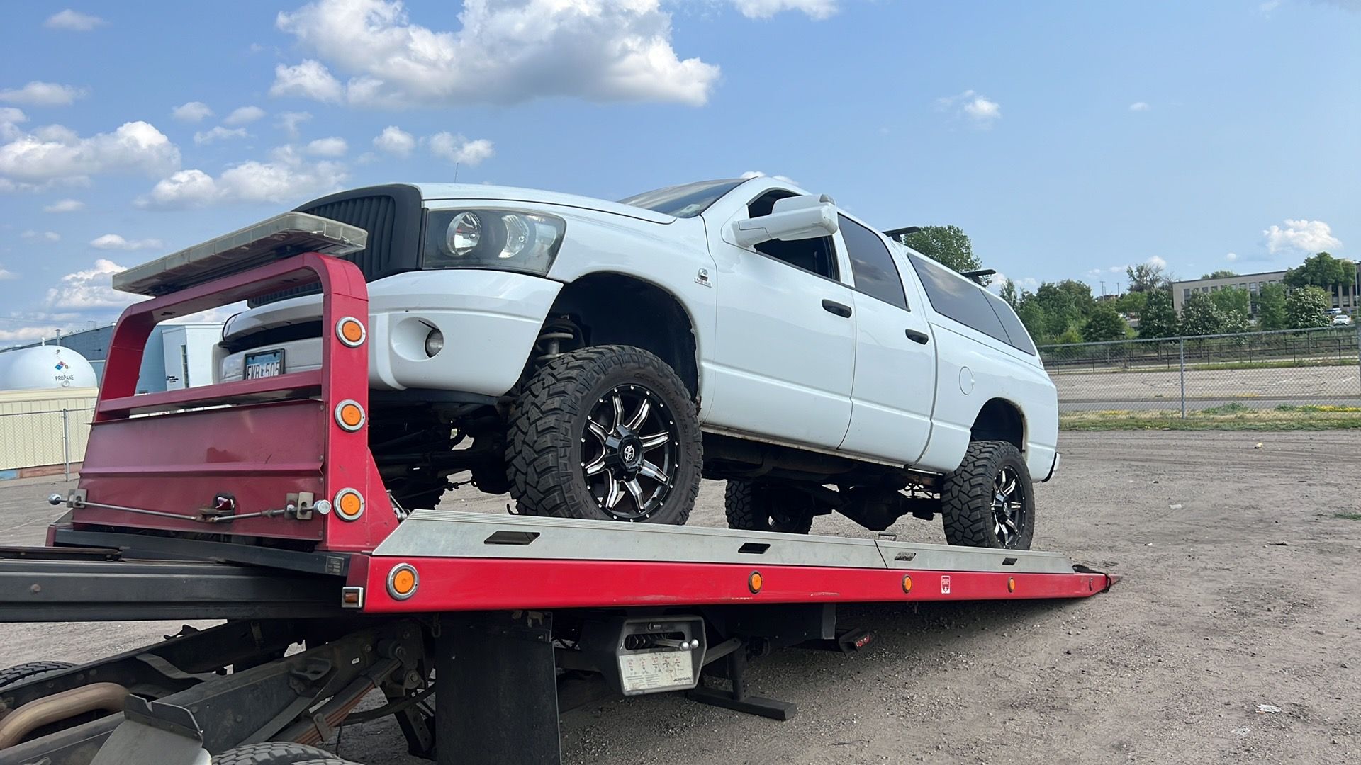 White pickup truck strapped on a red tow truck bed under a cloudy sky
