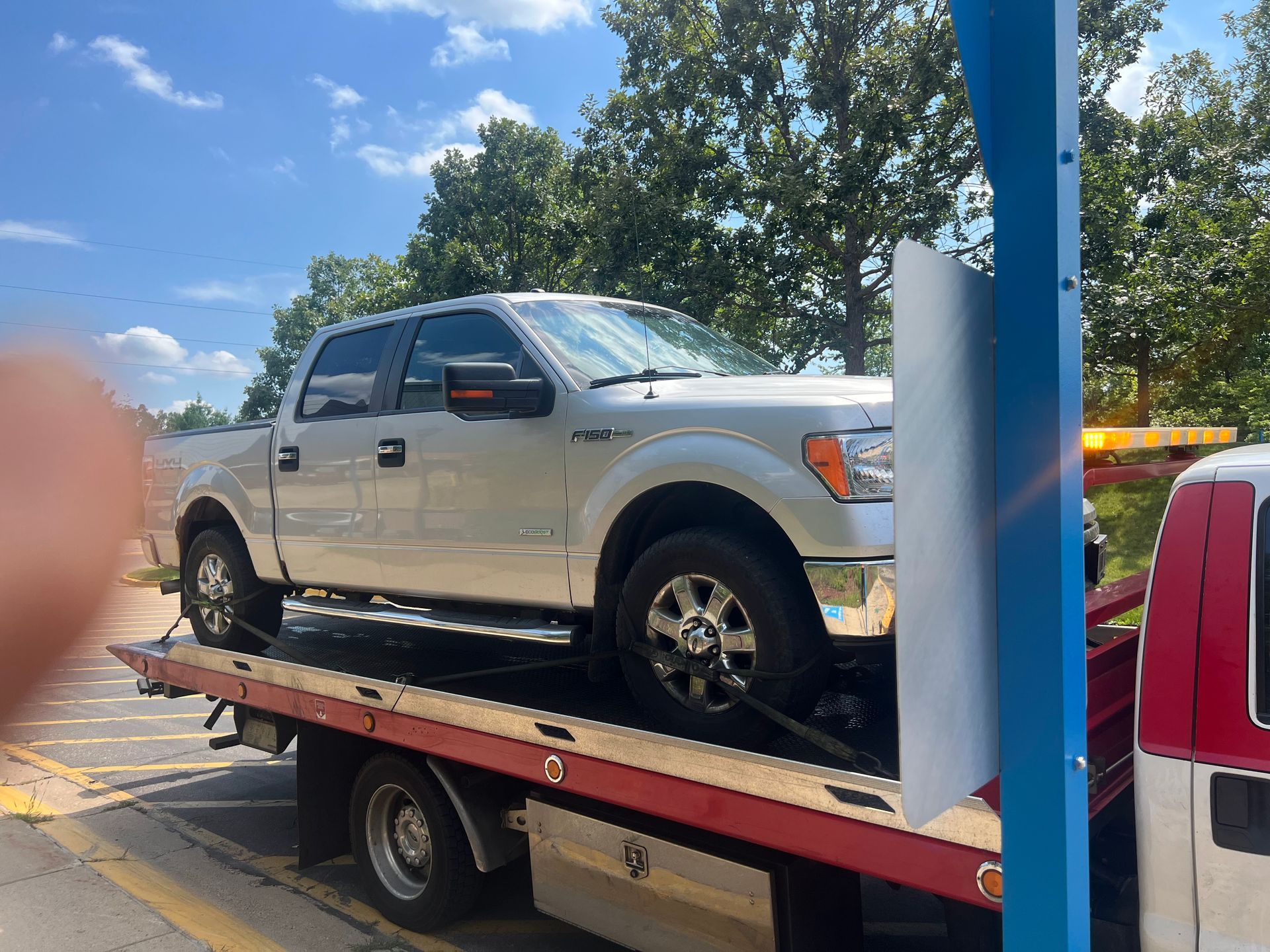 Silver pickup truck on a flatbed tow truck in a parking lot under a blue sky