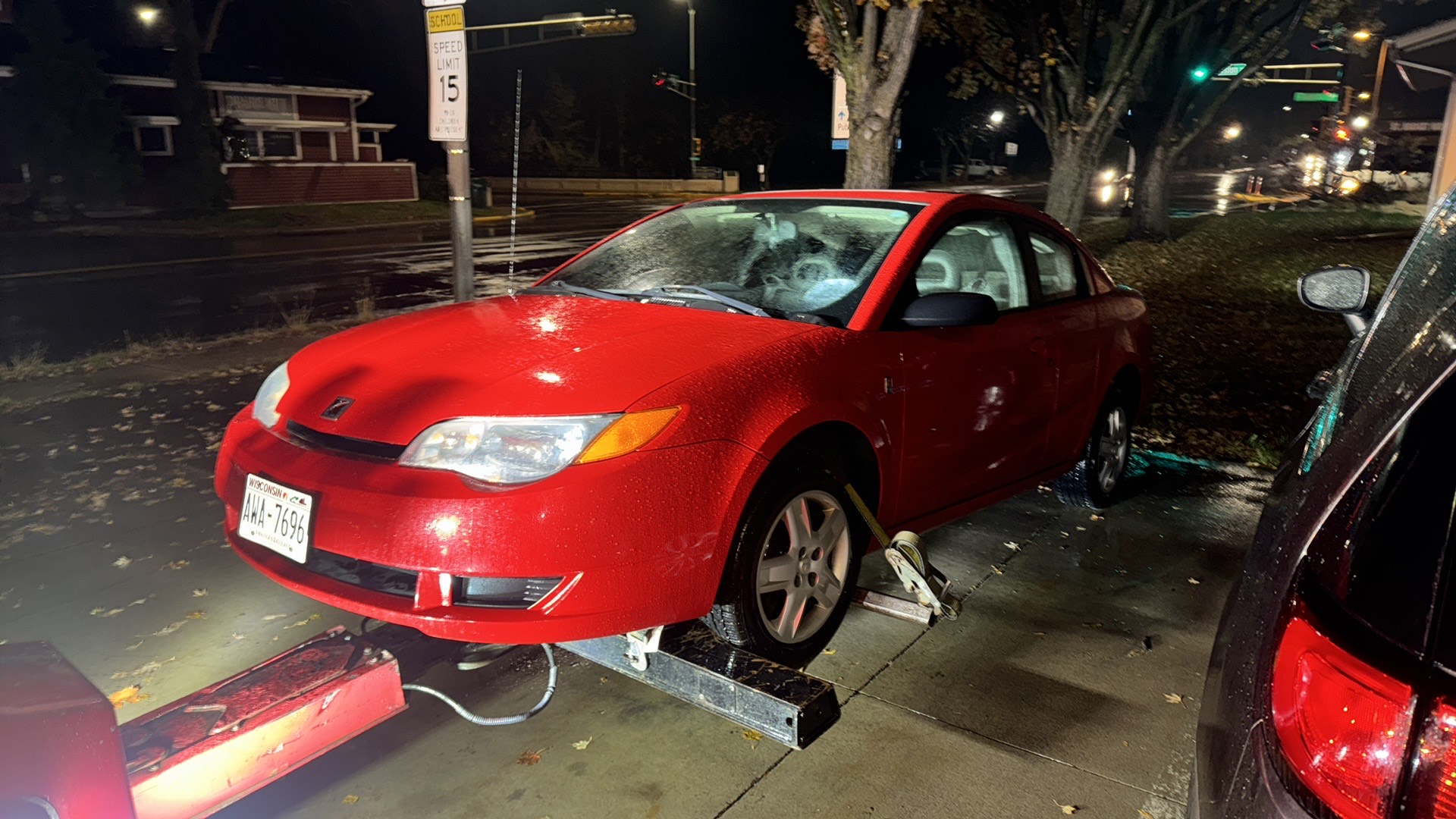 Red car with front-end damage at night, crashed onto a sidewalk with debris around it.