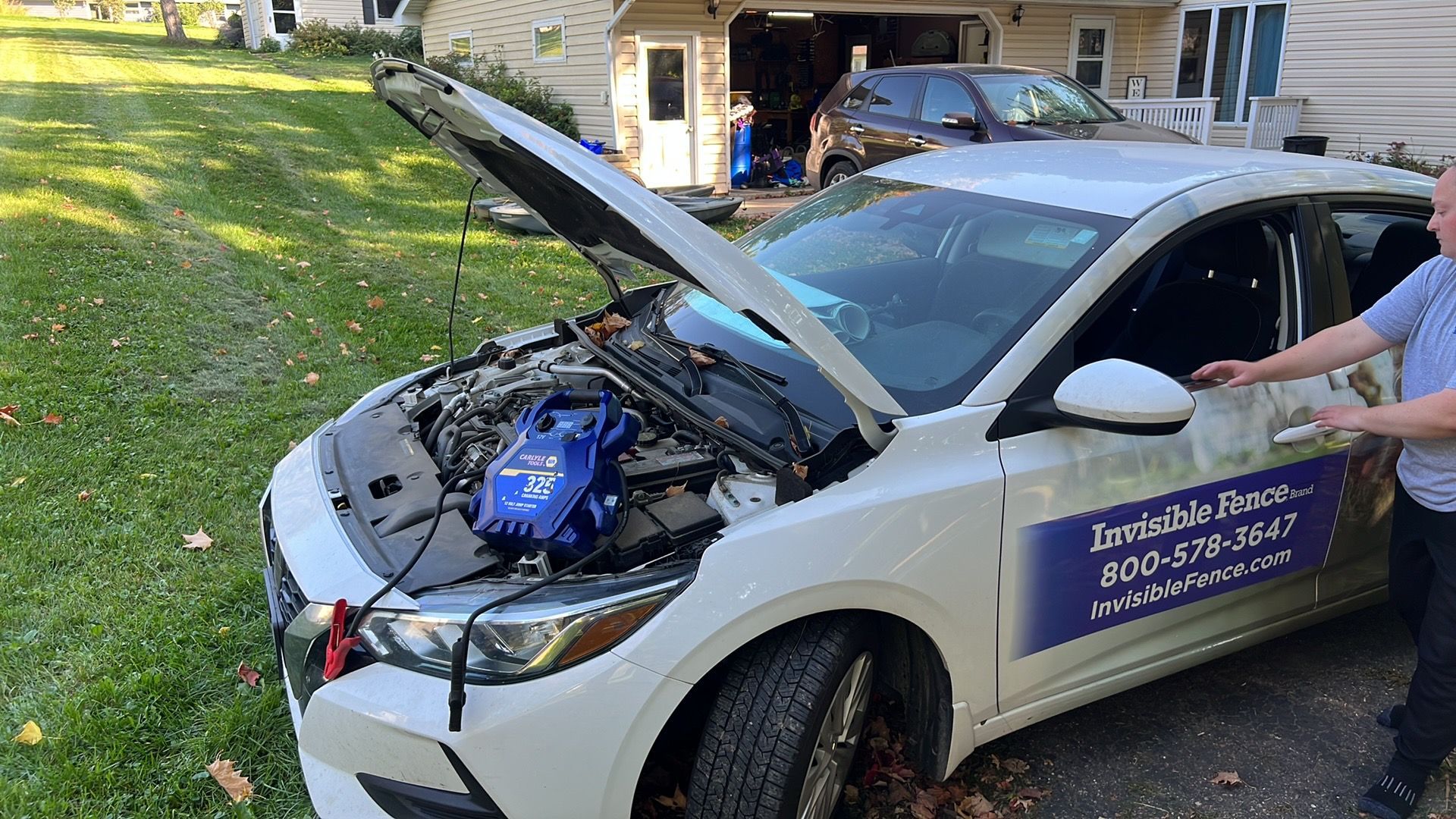 White car with hood open after a crash, showing front-end damage and a roadside assistance sign on the door