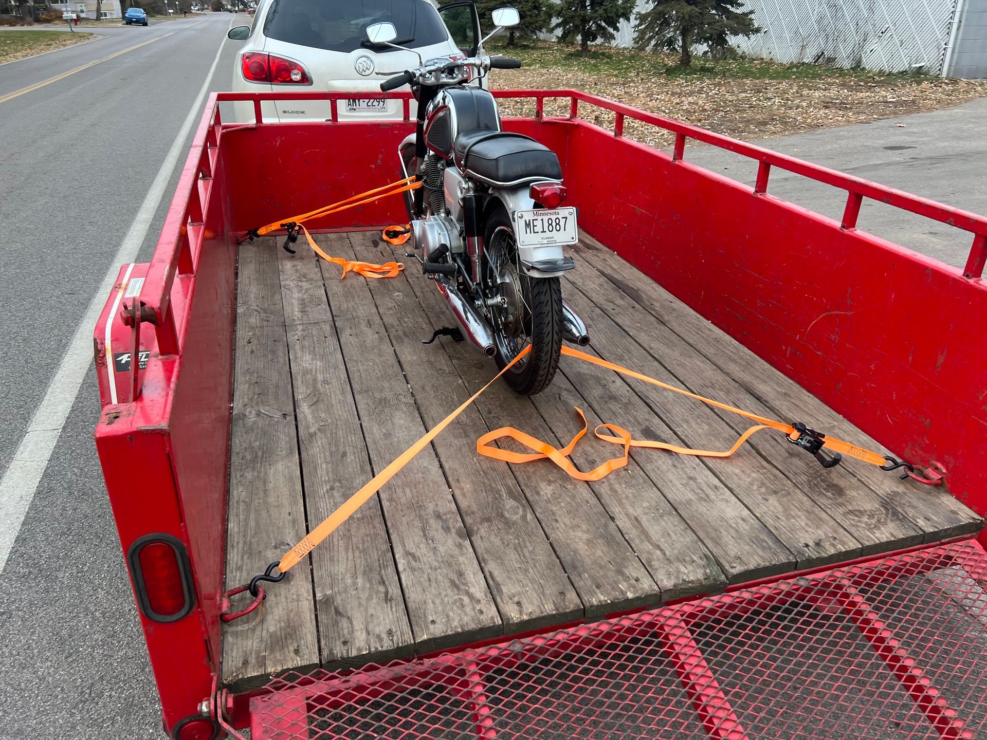 Motorcycle strapped in a red utility trailer on the roadside