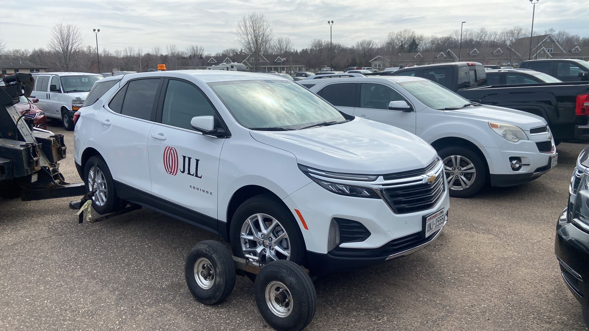 White SUV displayed on a dolly in a parking lot, with other vehicles nearby.
