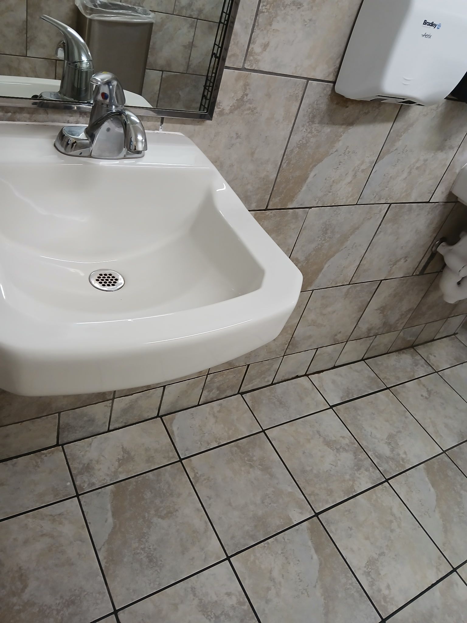 A wall-mounted white ceramic sink with a chrome faucet, set against beige tiled walls and a matching tiled floor.