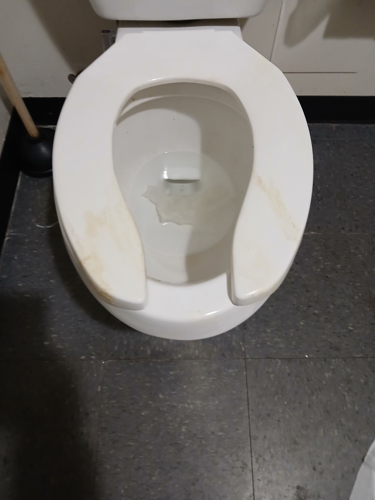 A top-down view of a white porcelain toilet with a stained seat against a dark gray tiled floor.