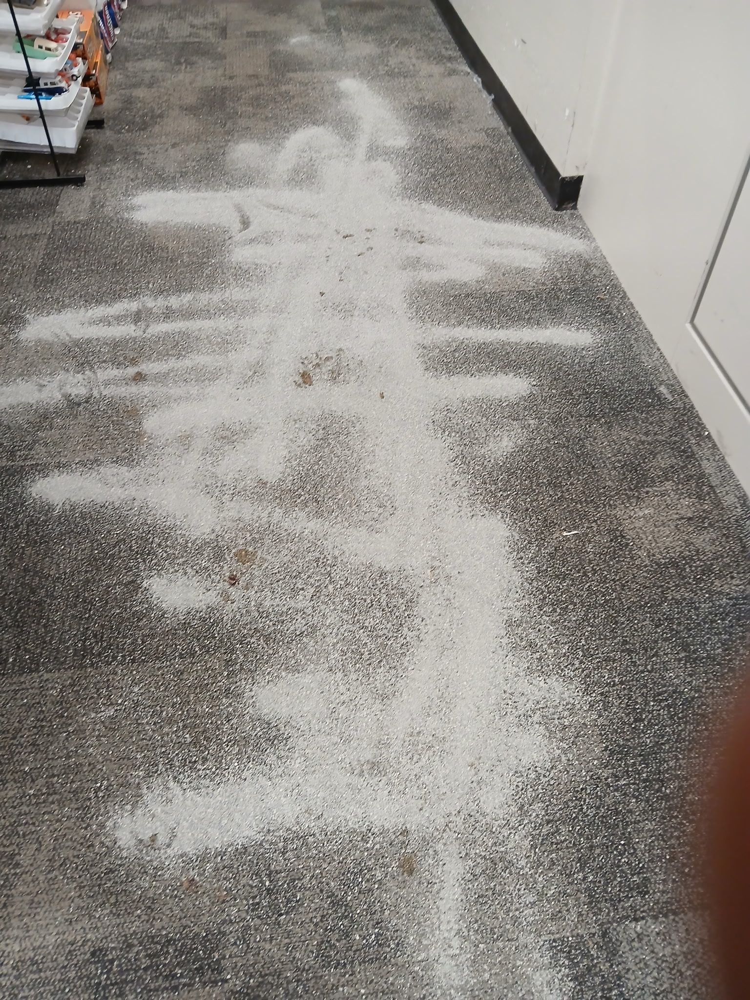 A white powdery substance is spilled on a textured gray floor, forming a large, irregular trail.
