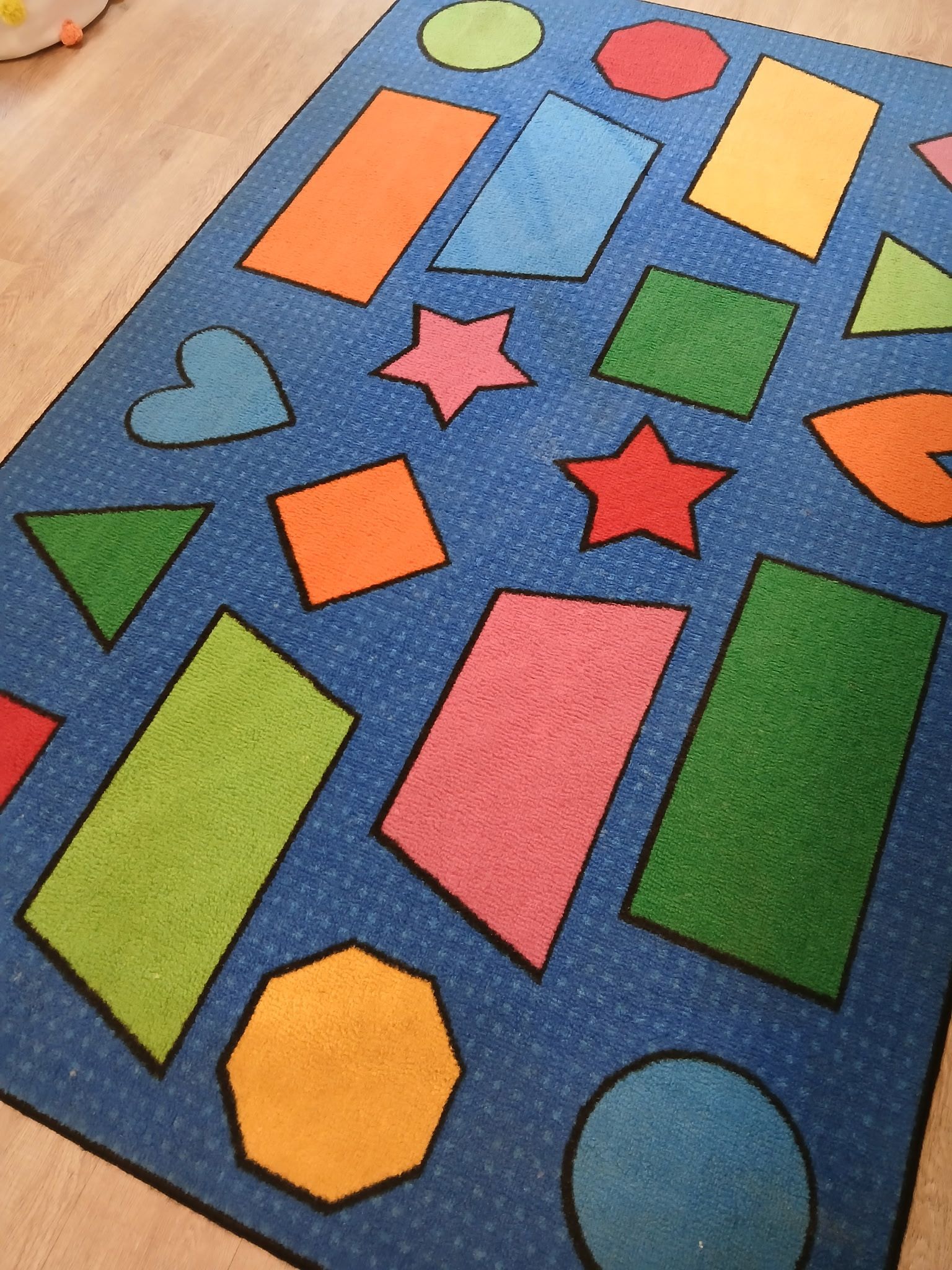 A blue rug decorated with various colorful geometric shapes, including rectangles, stars, triangles, and circles.