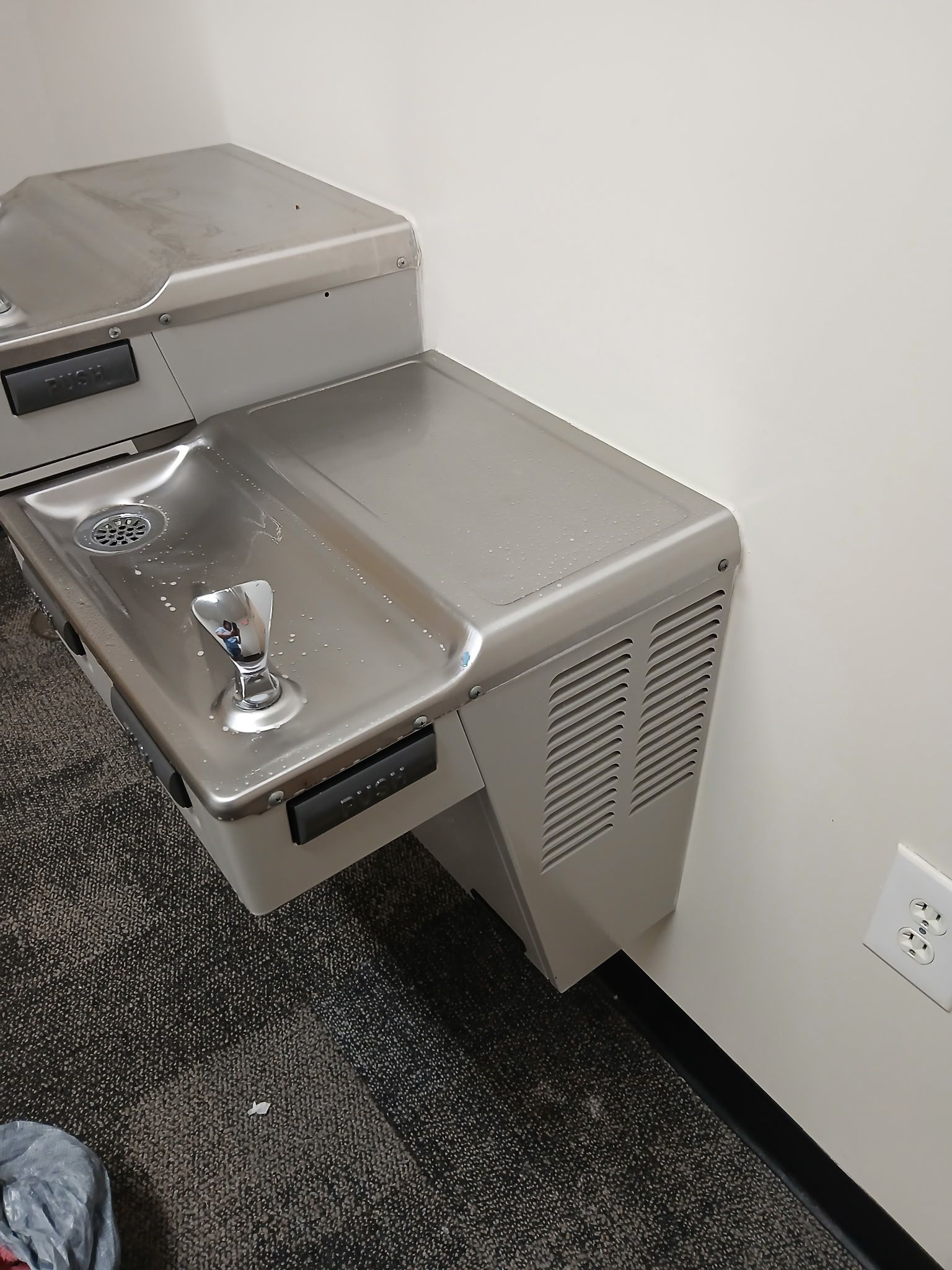 A wall-mounted, stainless-steel dual-level water fountain with a side-facing ventilation grille.