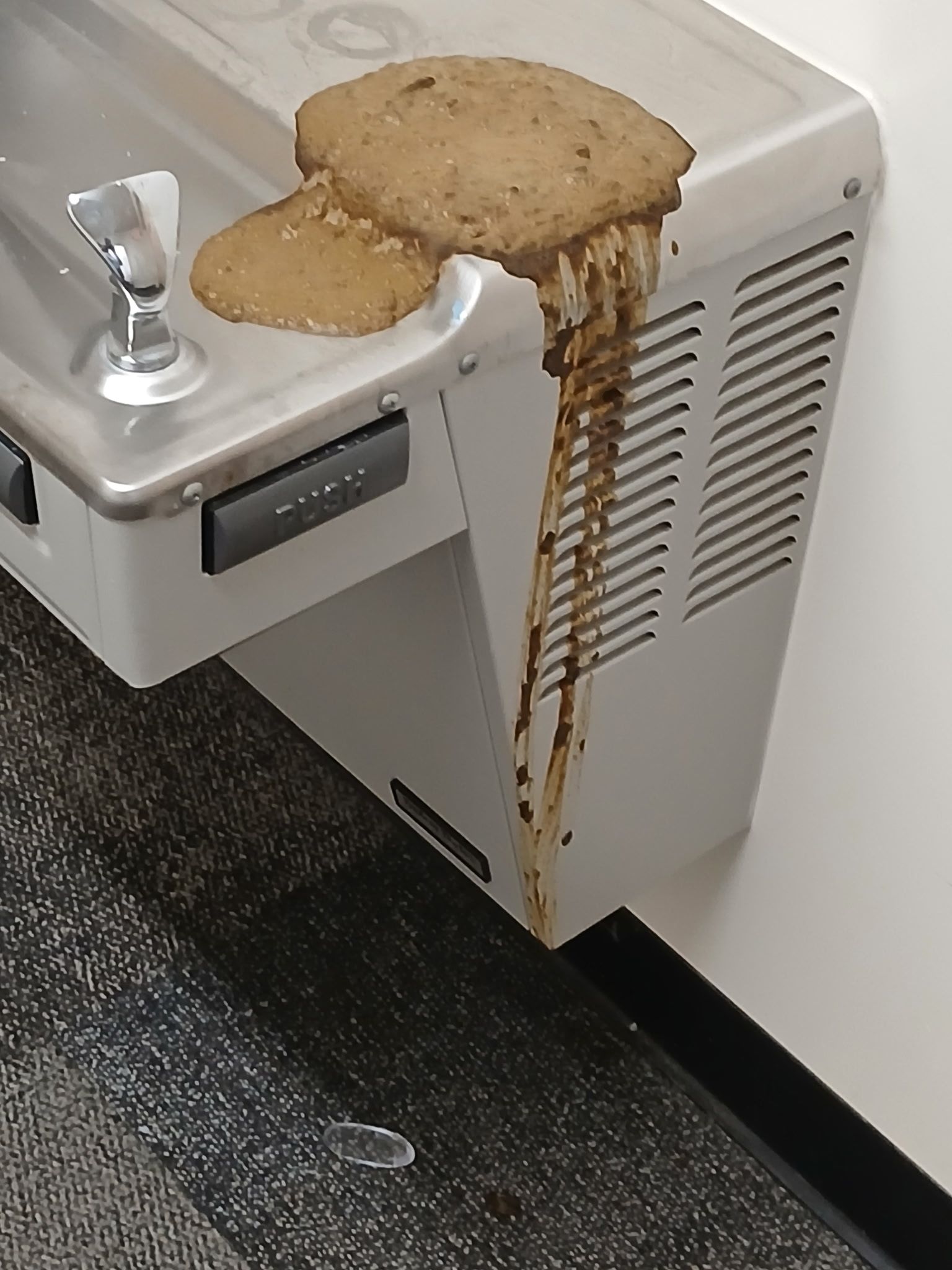 A half-eaten burger sits on a water fountain, with bits of food and sauce dripping down the front of the unit.