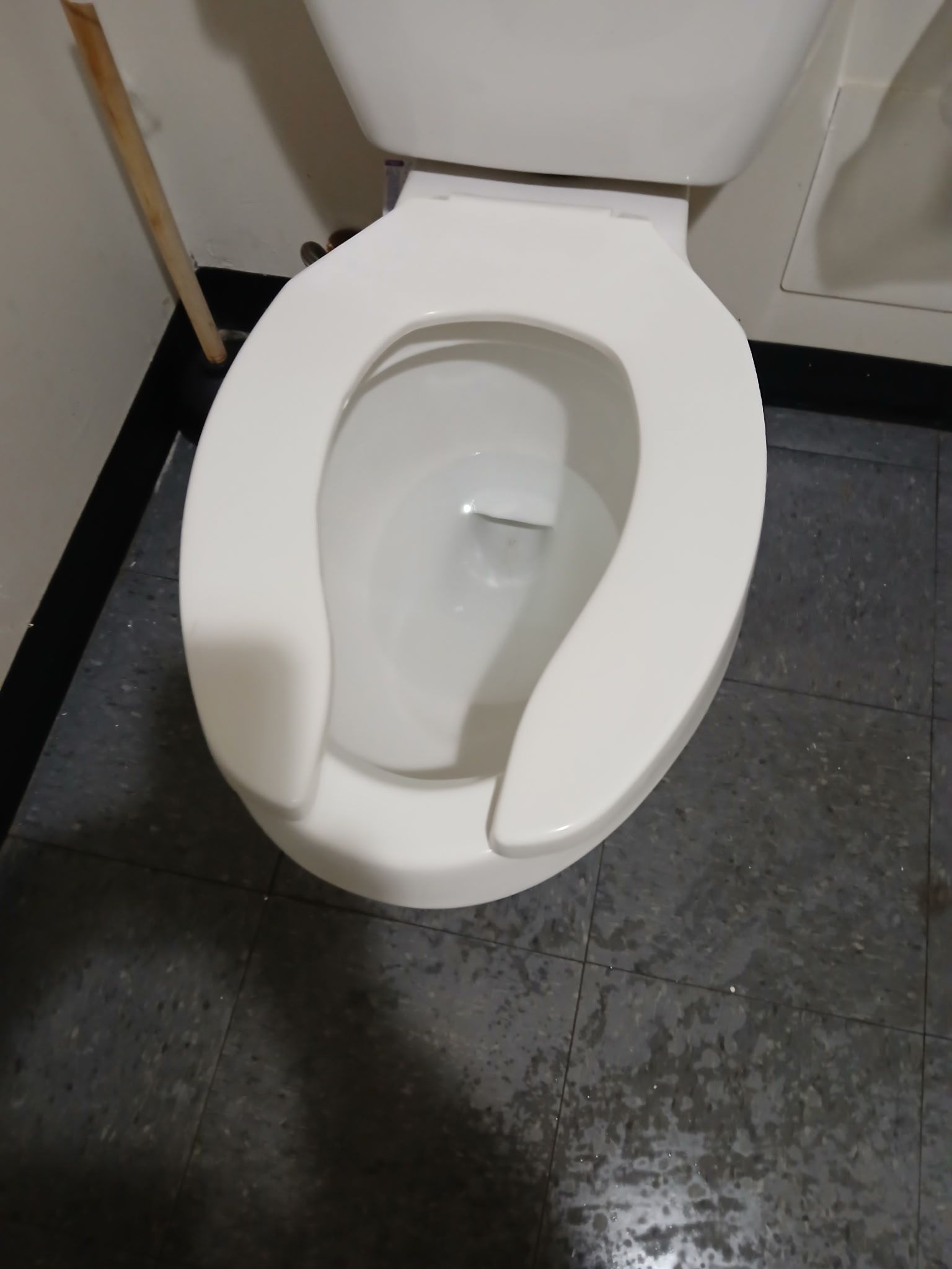A white porcelain toilet with an open seat sits in a room with grey tiled flooring and a wall-mounted grab bar.