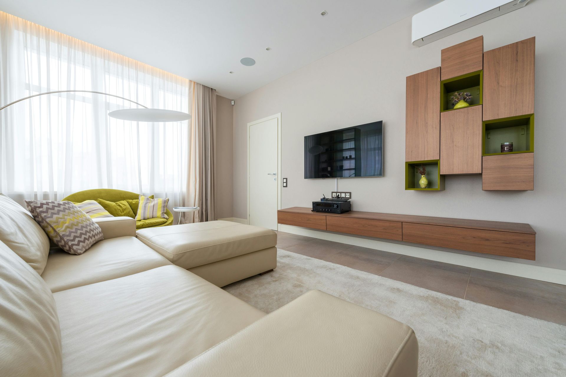 A modern living room with a white leather sectional, a floating wood media console, wall cabinets, and a television.