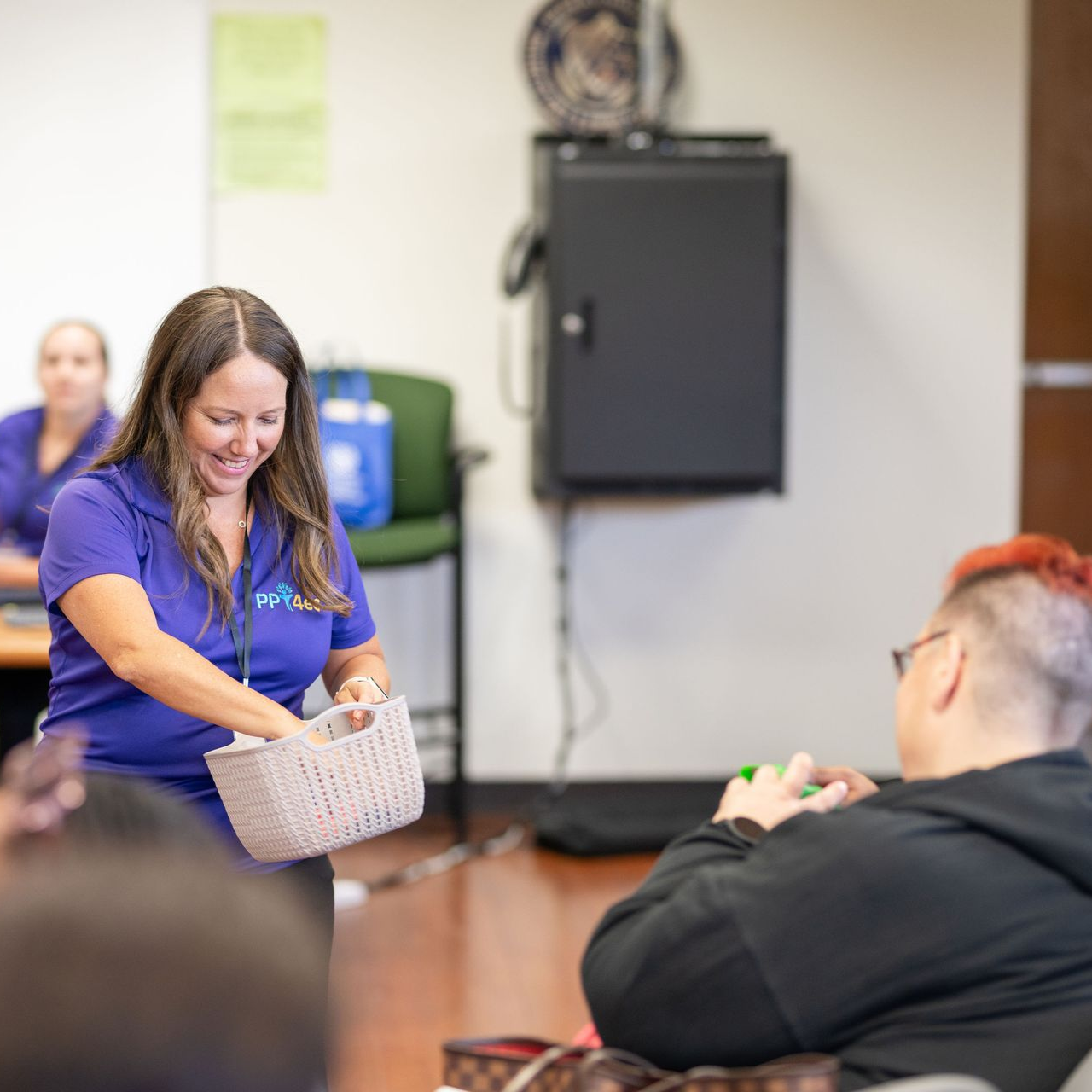 Children and adult sit on floor in circle, reading. Light blue carpet, white room.