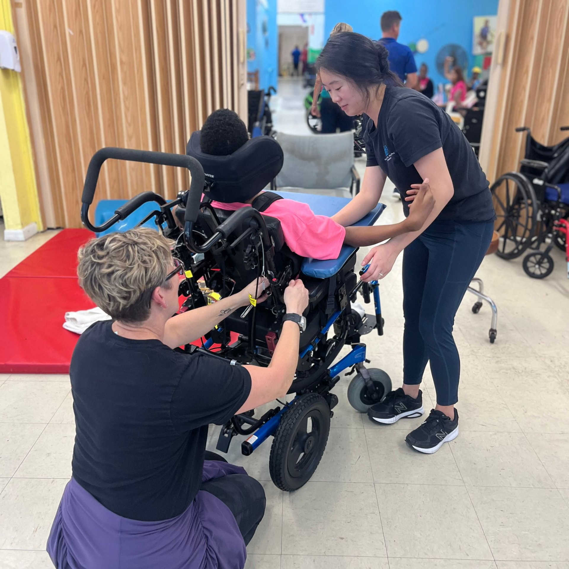 A woman with a clipboard leads a discussion with a small group of children seated in a circle.