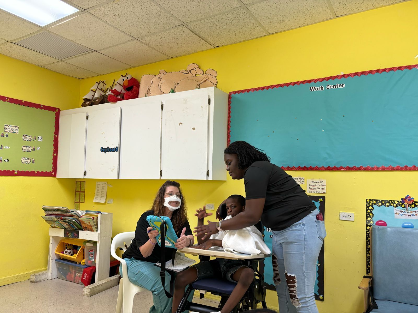 A woman is helping a child with a tablet in a classroom.