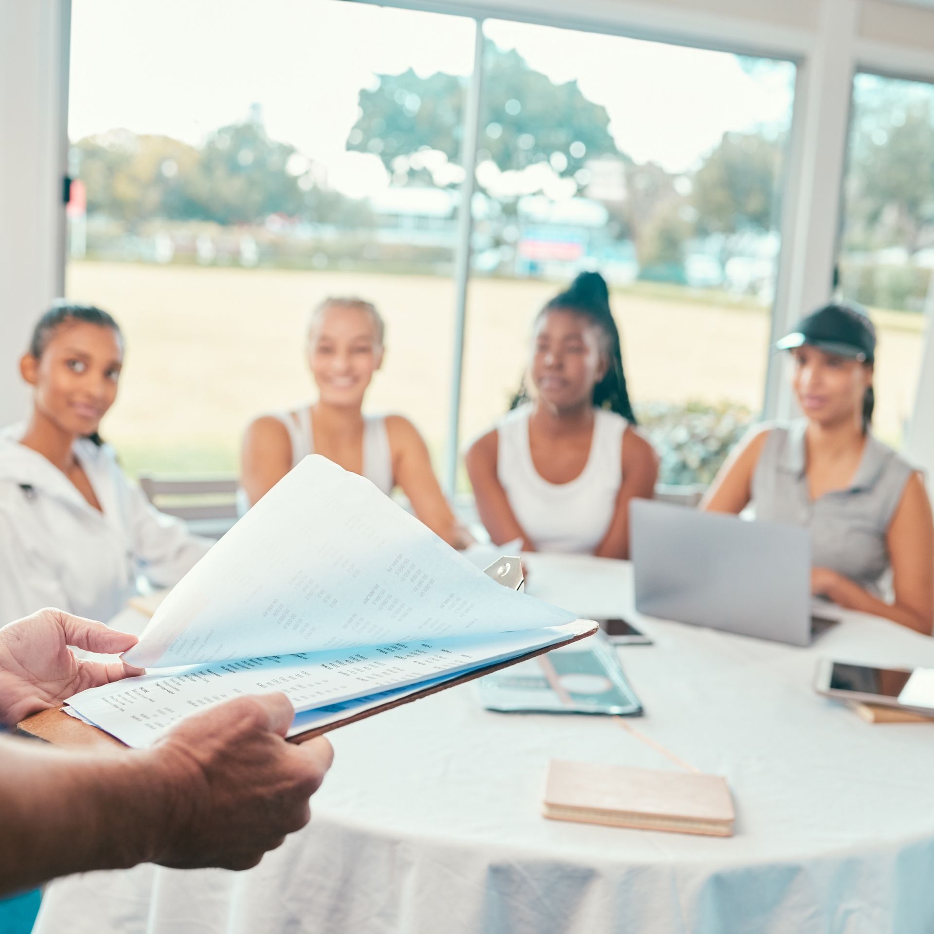 A person is holding a piece of paper in front of a group of people sitting around a table with laptops.