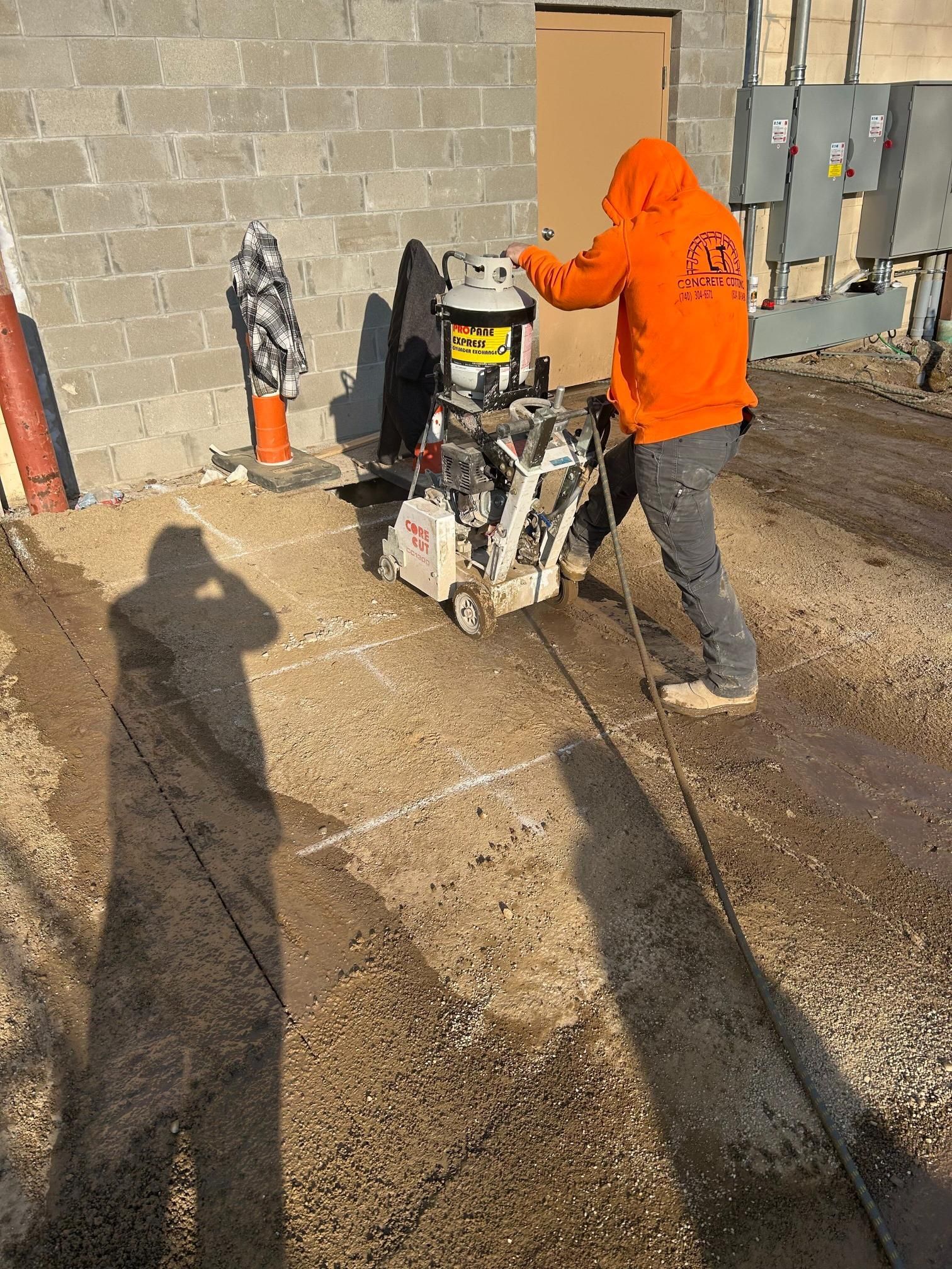 A man in an orange hoodie is using a machine to cut concrete.