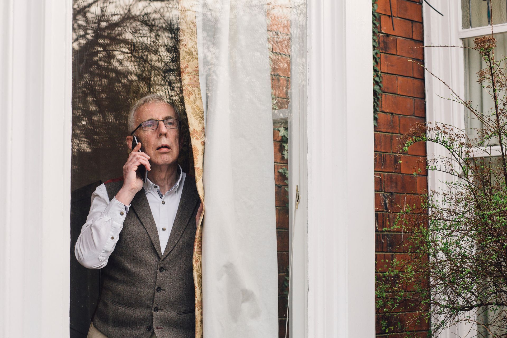 A man is standing in front of a window talking on a cell phone.