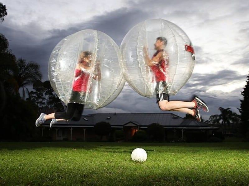 Two people are playing soccer in bubbles in a field