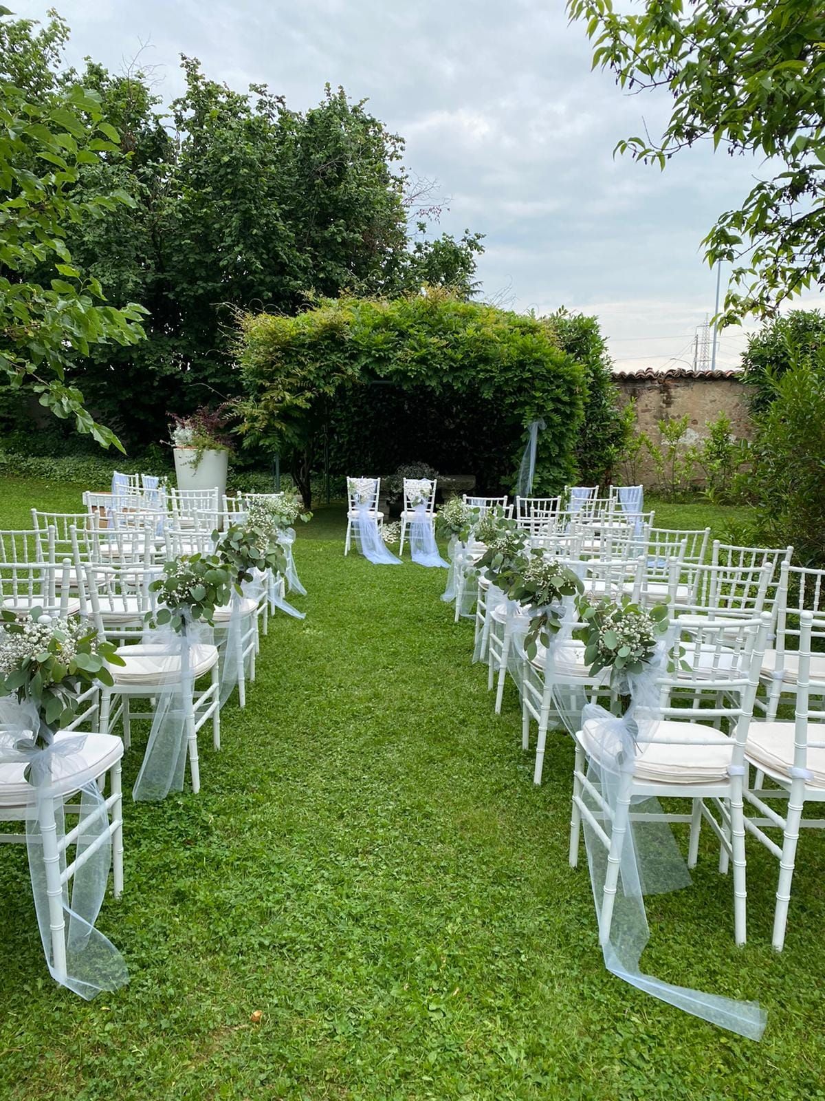 Una fila di sedie bianche è allineata in un campo erboso per una cerimonia nuziale.